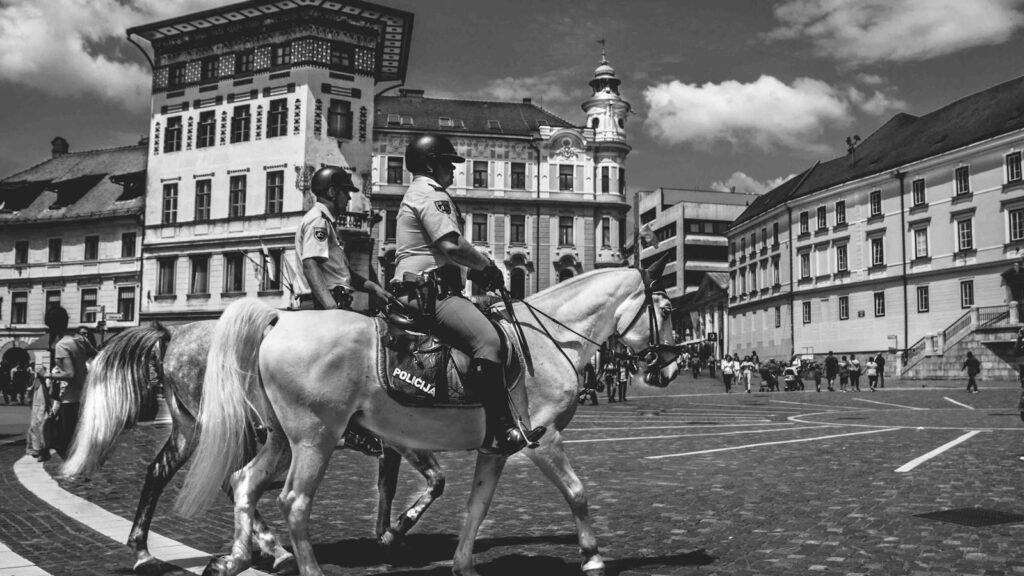 Black and white photo of mounted police on horses in a historic city square.