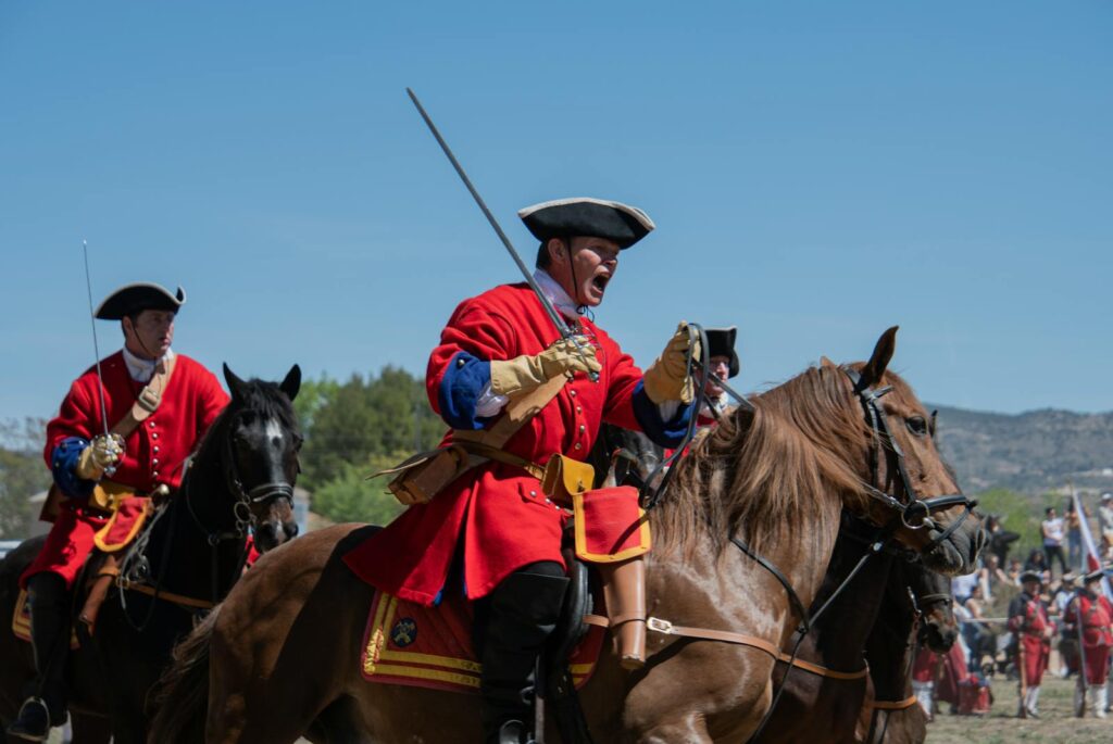 Men in historical uniforms engage in a dramatic battle reenactment on horseback.