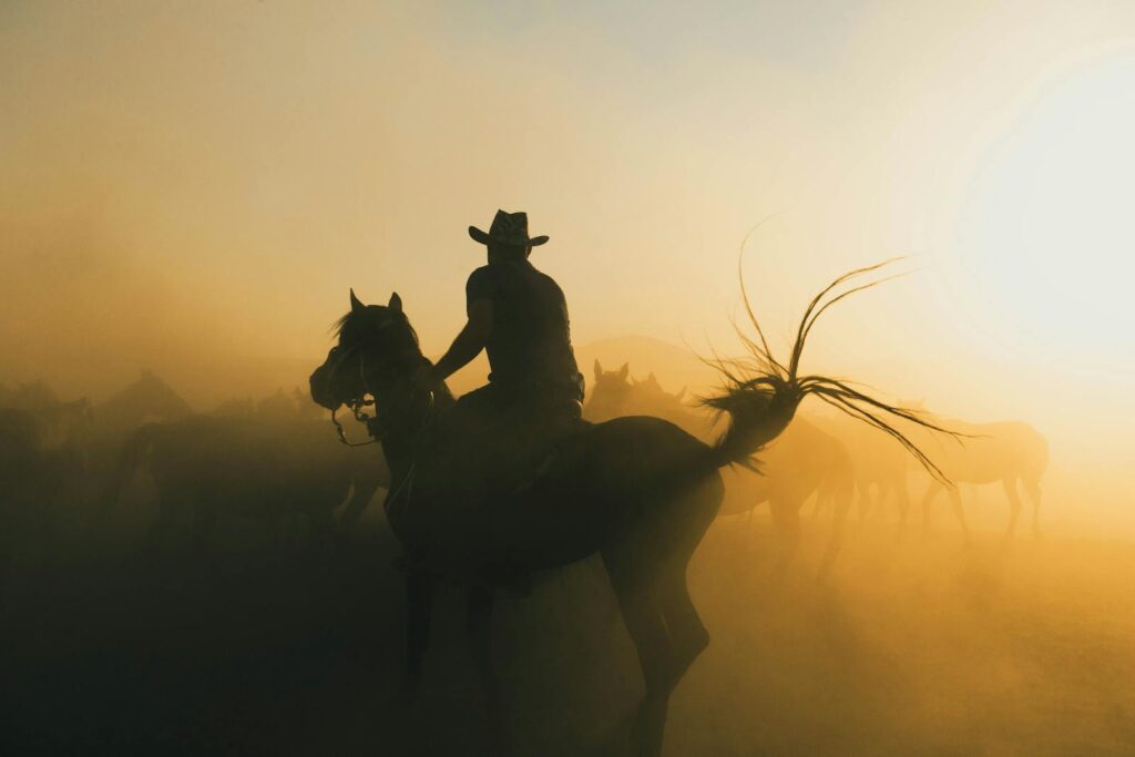 Cowboy riding a horse through a dusty sunrise