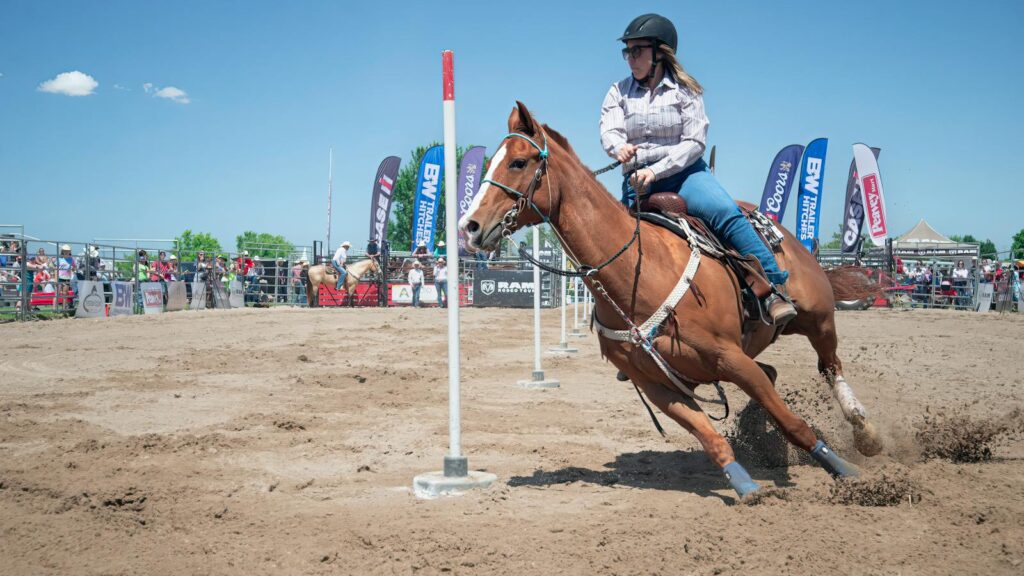 Woman in a rodeo event on horseback navigating poles outdoors.