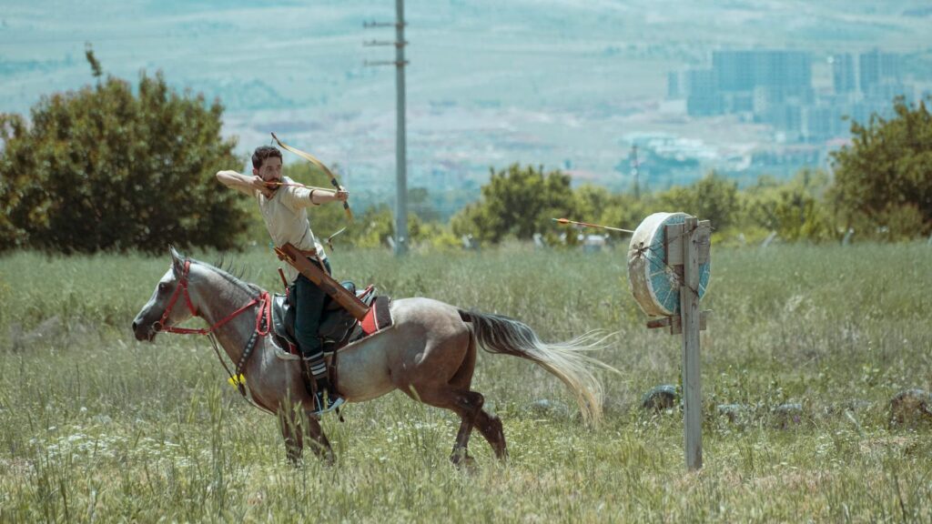 A skilled archer on horseback aiming at a target in picturesque Turkish landscape.