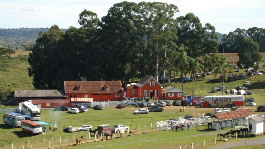 Aerial view of a ranch with vehicles, parked cars, horses, and trees in a rural setting.