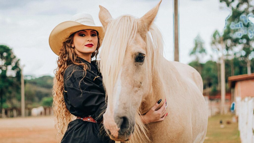 A woman in cowboy hat embraces a perlino horse on a scenic farm.