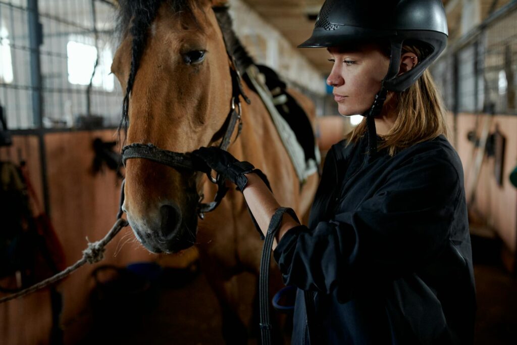 Woman in riding gear bonding with her horse inside a stable.