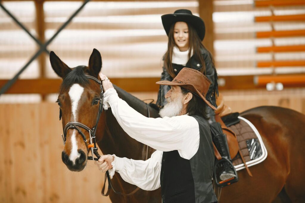 Grandfather helps his granddaughter learn horseback riding in a stable