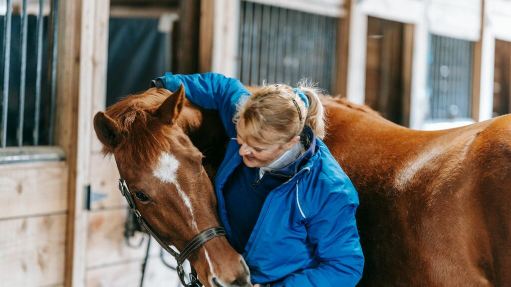 A woman lovingly embraces a horse in a rustic stable setting, showcasing equestrian care and bonding.