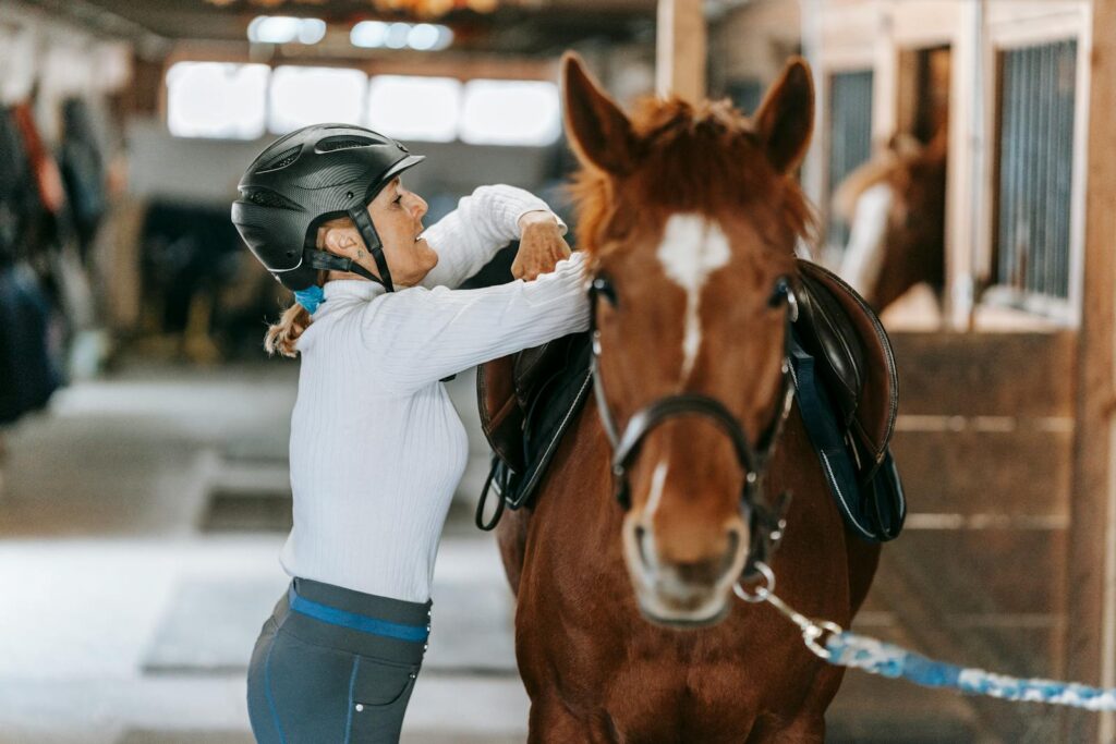 A woman prepares her horse in an indoor stable, showcasing equestrian skills.