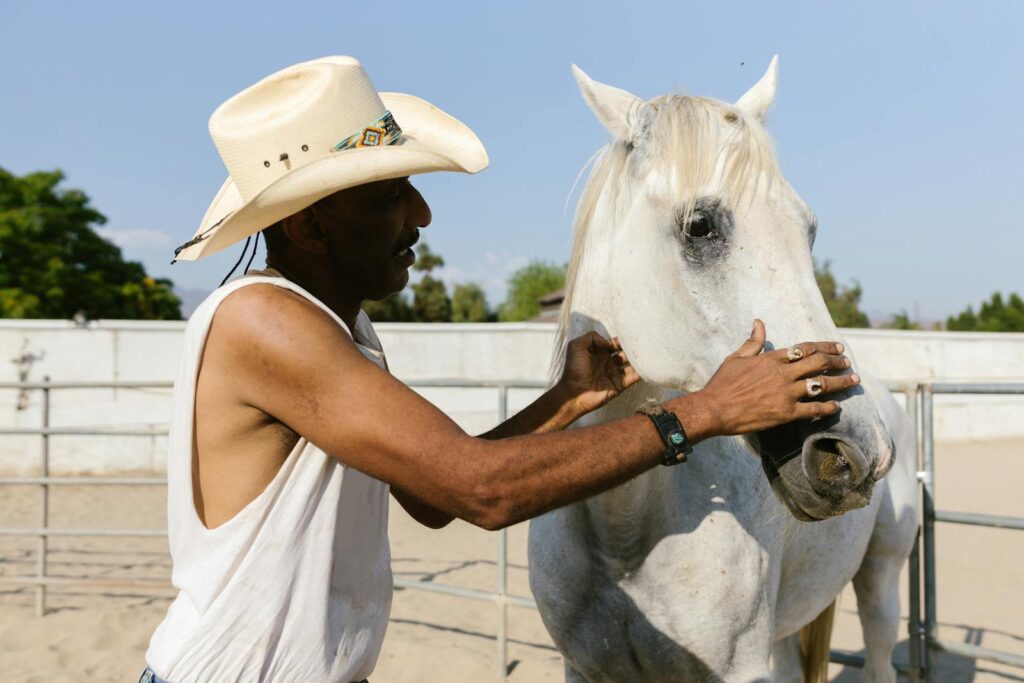 Cowboy wearing hat bonding with a white horse outdoors