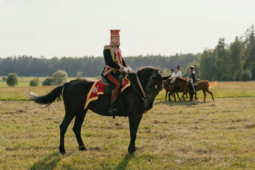 A cavalry soldier in vintage uniform on horseback during a napoleonic reenactment in a grassy field.