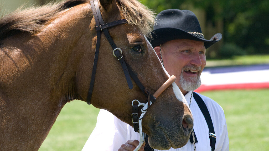A ranch hand is smiling with his horse