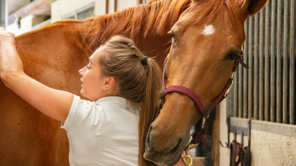 woman in white crew neck t-shirt standing beside brown horse during daytime