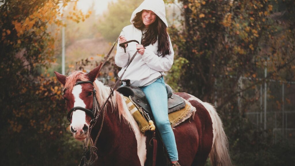 woman in white long sleeve shirt riding brown horse during daytime