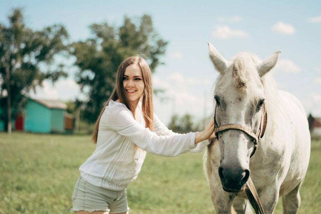 Woman leading white horse in a sunny day