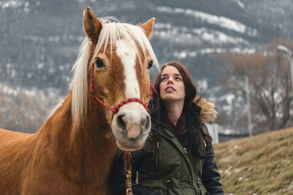 Woman in green jacket standing beside brown horse