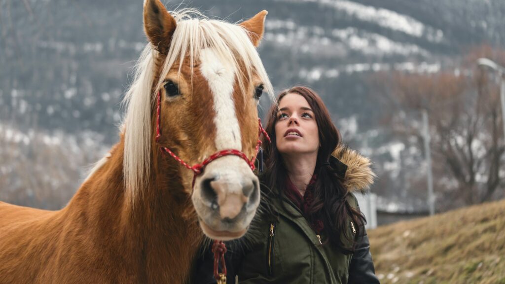 woman in green parka jacket standing beside brown horse