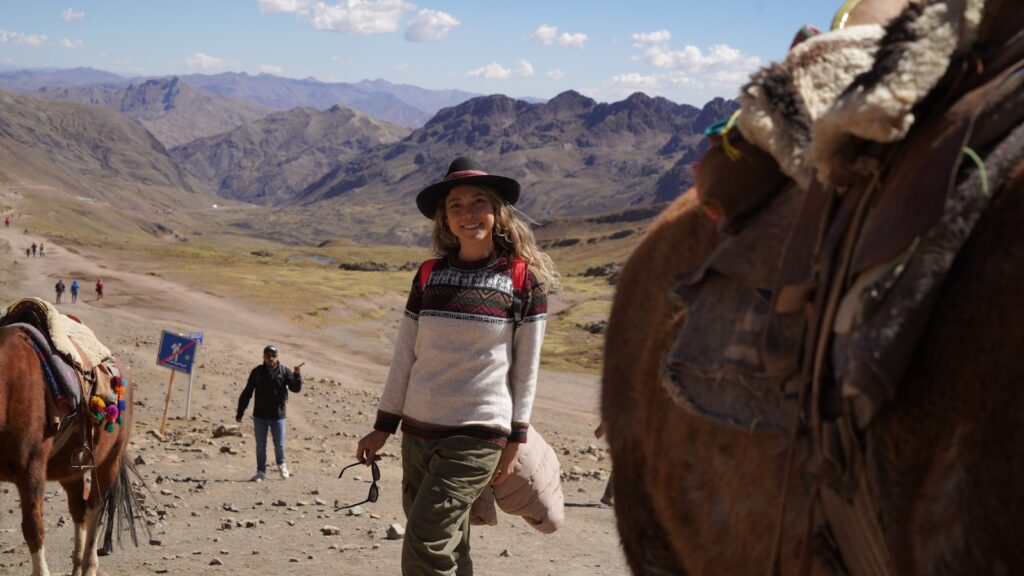 A woman walking down a dirt road next to a brown horse