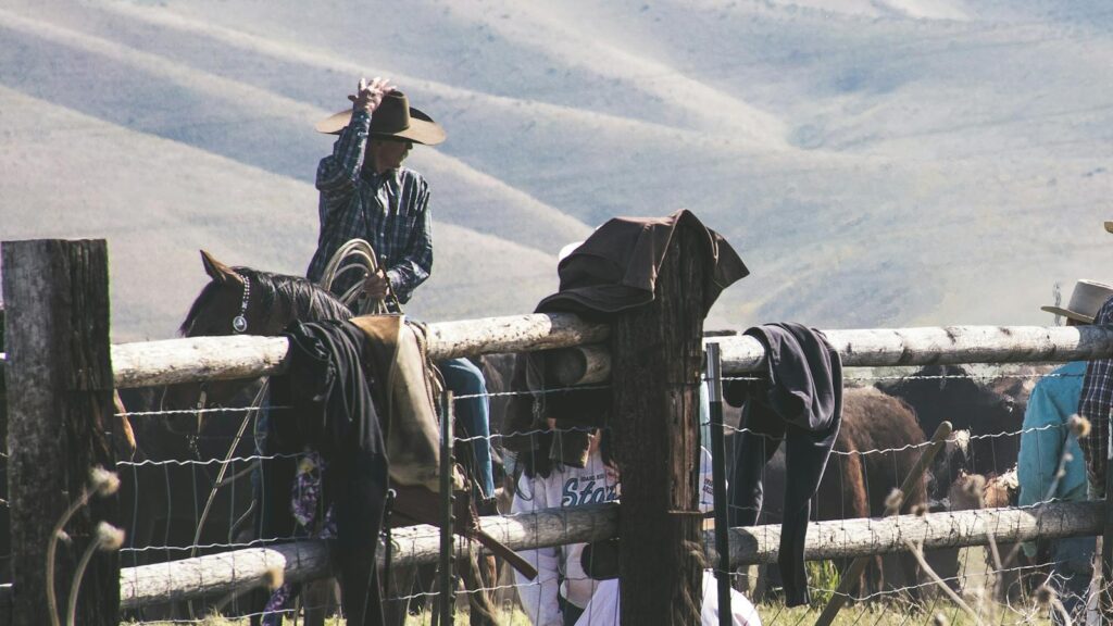 Cowboy riding horse on a rural farm with mountains in the distance.