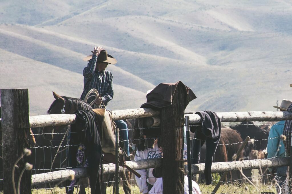 Cowboy riding horse on a rural farm with mountains in the distance.