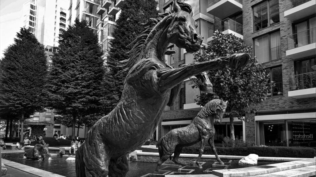 Black and white photo of dynamic horse statues in a modern urban park.