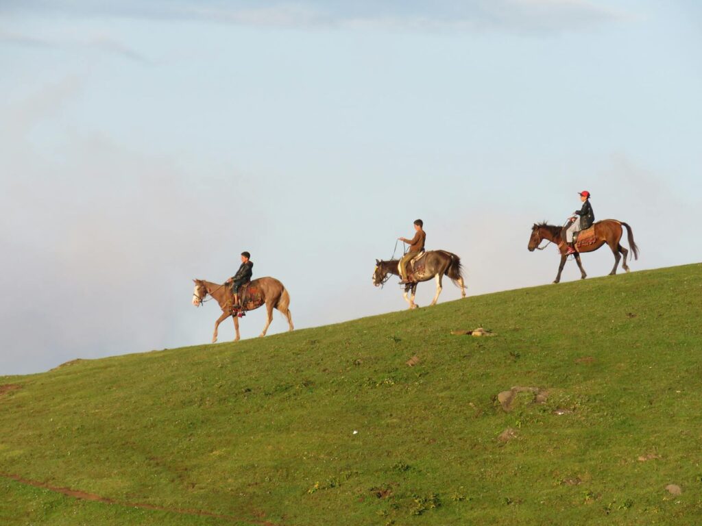 Three horse riders traveling across a grassy hill under a clear sky