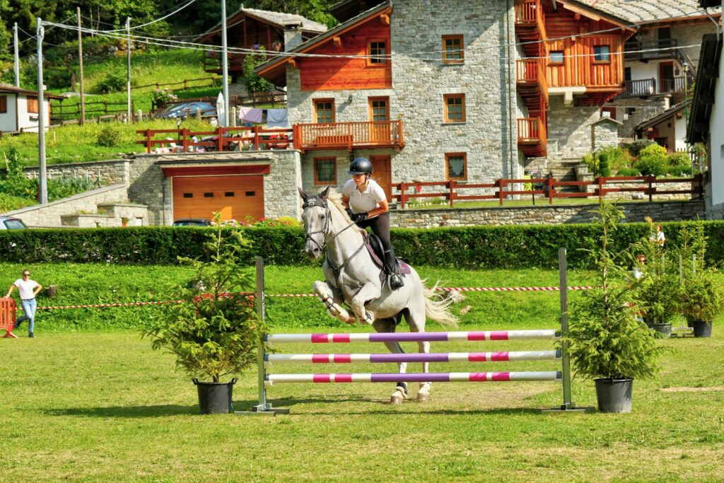 Rider and horse jump hurdles in scenic Italian village setting.