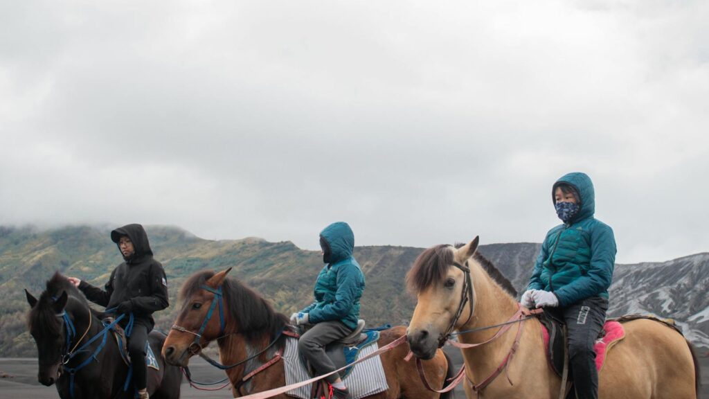 People horseback riding in scenic mountainous area under cloudy skies.