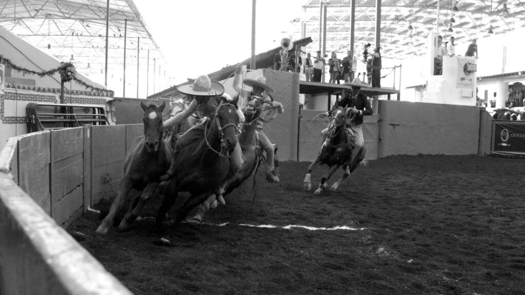 Exciting horse racing action captured in black and white at an indoor arena with jockeys and audience.