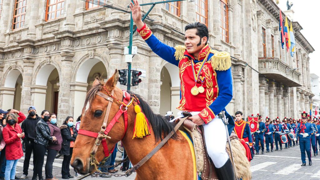 A vibrant parade in Ecuador featuring traditional costumes and horsemen waving to the crowd.