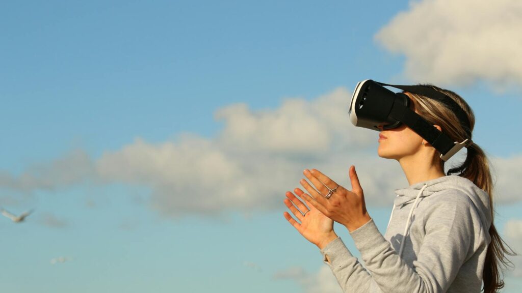 Woman using VR headset outdoors, exploring virtual reality under a clear blue sky.