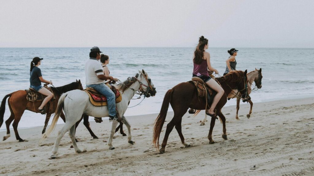 Group of people enjoying horseback riding along Bucerías beach, Mexico, against ocean waves.