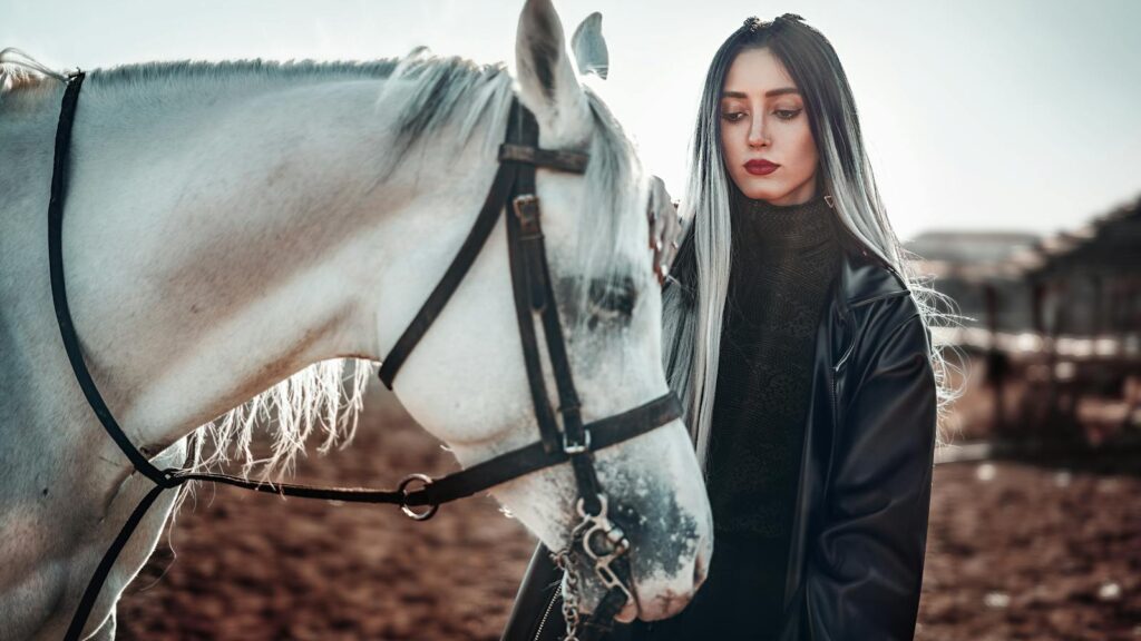 A fashionable woman in a black leather jacket poses with a white horse outdoors in Ardabil, Iran.