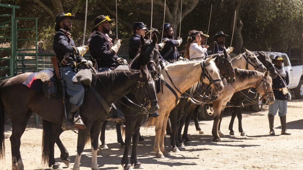 Group of soldiers on horseback in historical military uniforms ready for action under trees.
