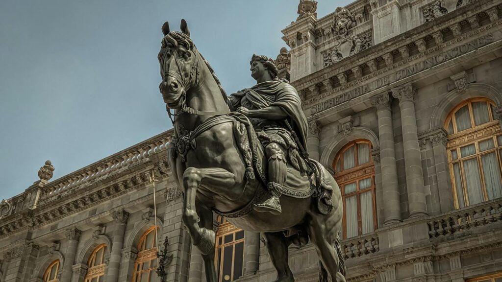 Low-angle view of an equestrian statue in front of an ornate historic building in Mexico City.