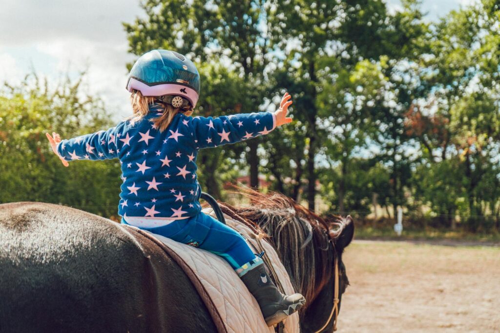 Child confidently rides a horse outdoors