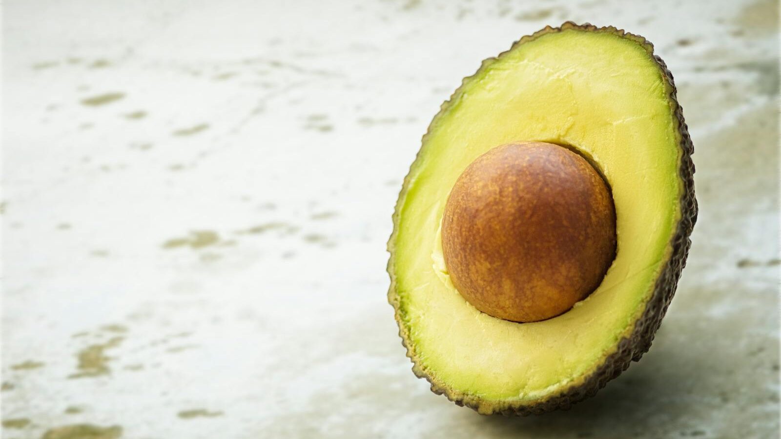 Close-up of a ripe avocado half with seed, showcasing its vibrant green flesh on a soft textured background.