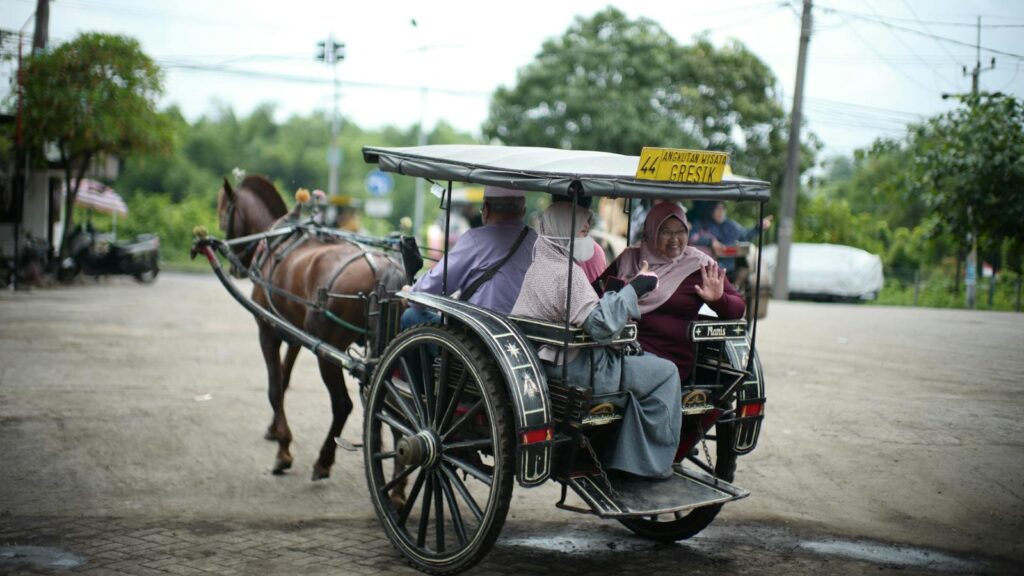 People enjoying a horse carriage ride on the streets of Gresik, Indonesia, featuring local sights.