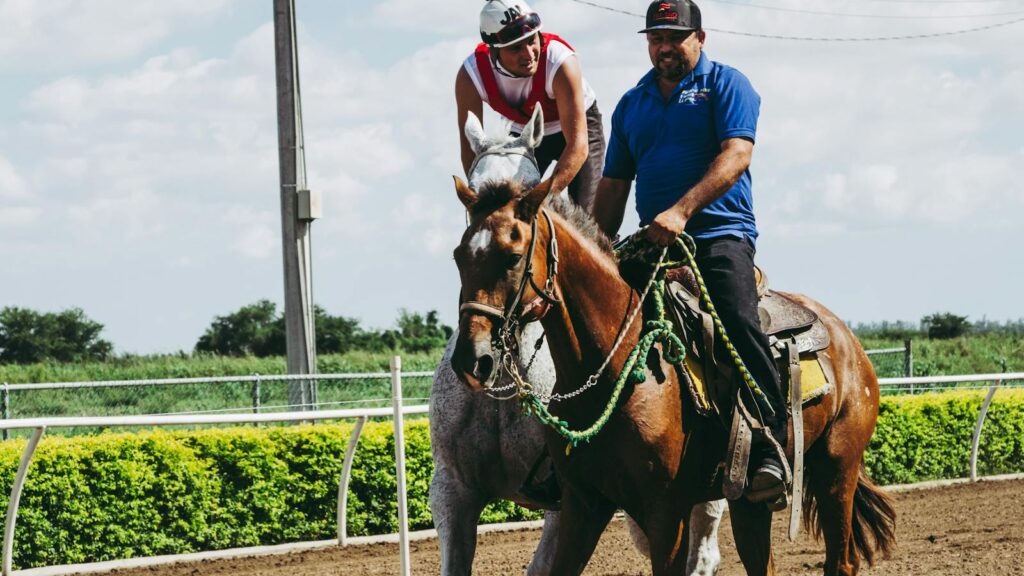 Two men enjoying horseback riding at a sunny racetrack, showcasing leisure and happiness.