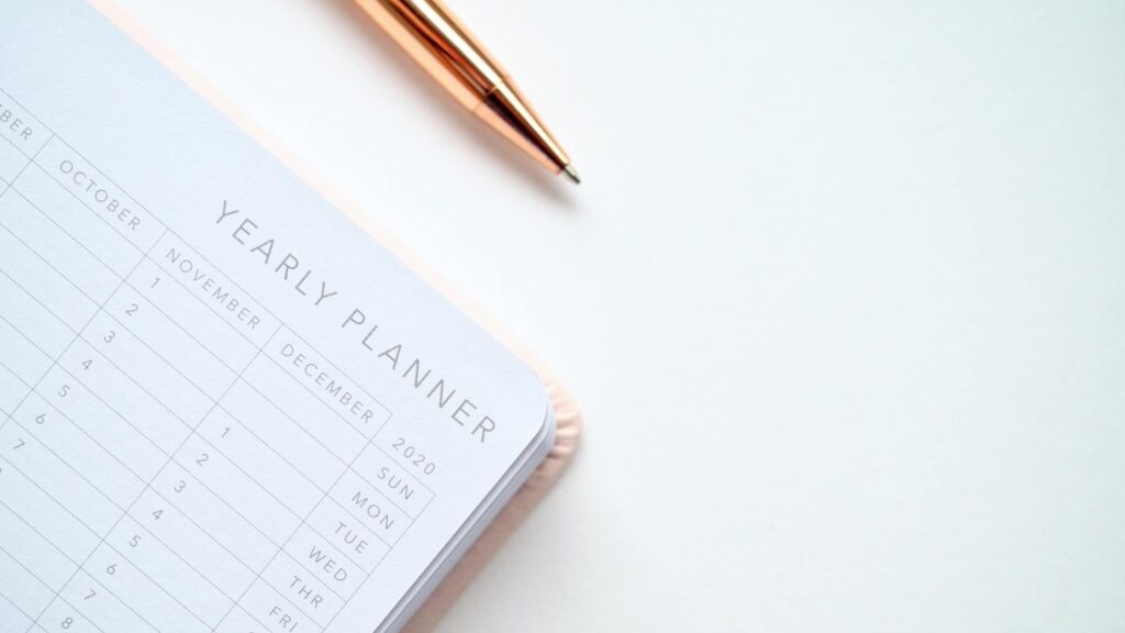 A stylish yearly planner open to a 2020 calendar page, accompanied by a golden pen on a clean white surface.