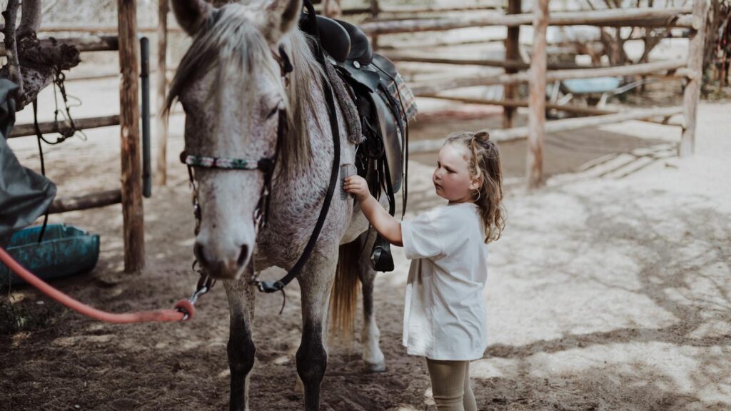 A young girl interacts with a horse at a charming rural ranch setting, capturing a tender moment.