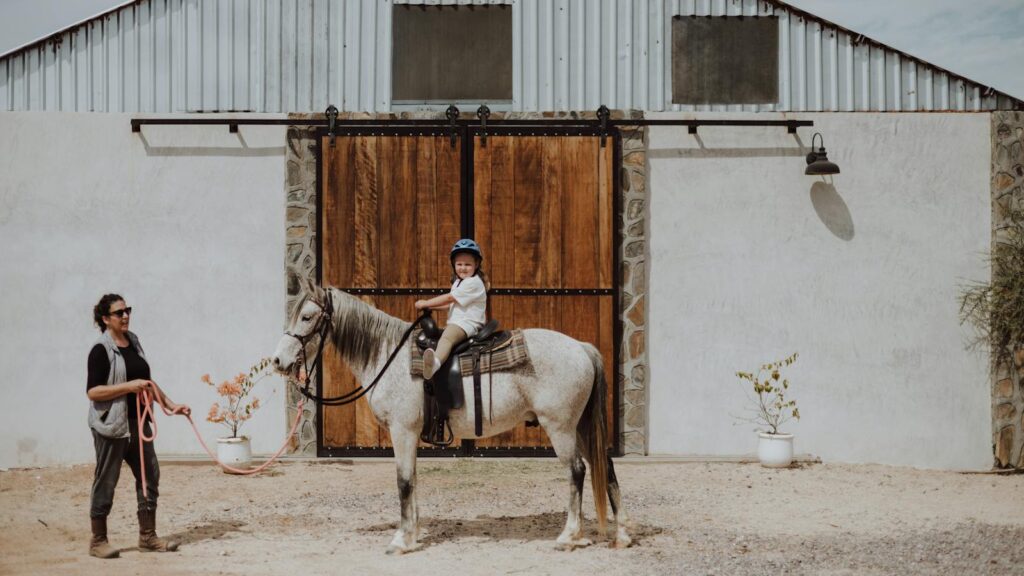 A young girl rides a horse with her mother nearby at a farm in San Juan del Rancho, Mexico.
