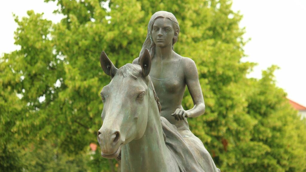 A detailed bronze sculpture of a woman riding a horse in a lush green park setting, perfect for outdoor art collections.