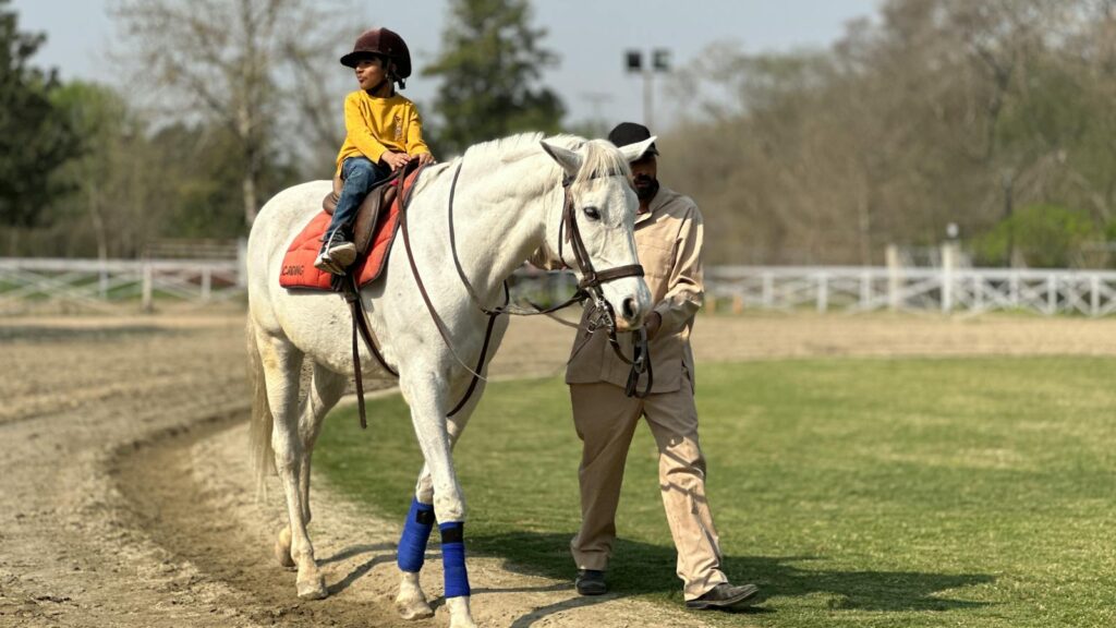 A young child enjoys a horseback ride with guidance in a serene Islamabad park setting.