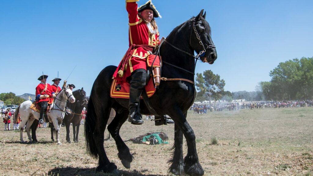 A vivid scene of a historic military reenactment featuring soldiers on horseback in colorful uniforms.