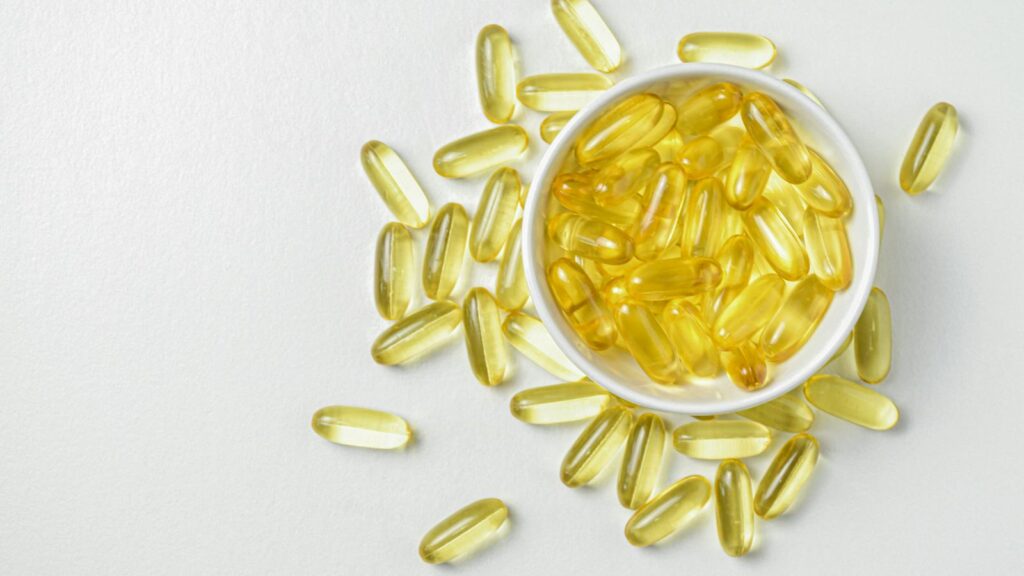 High-angle shot of omega-3 fish oil capsules in a ceramic bowl on a white background.