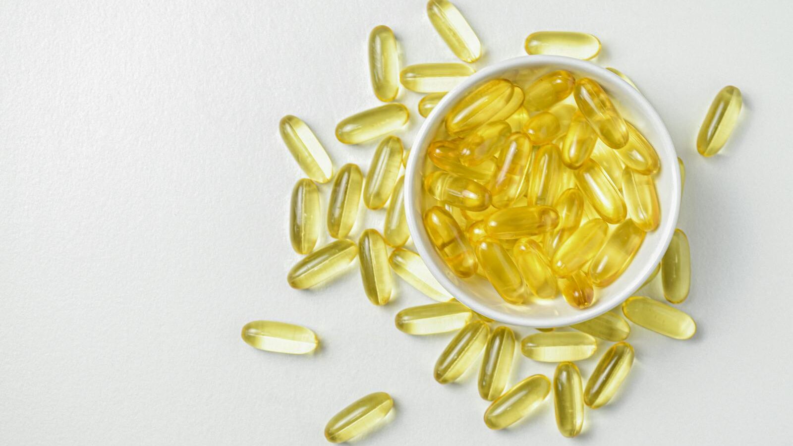 High-angle shot of omega-3 fish oil capsules in a ceramic bowl on a white background.