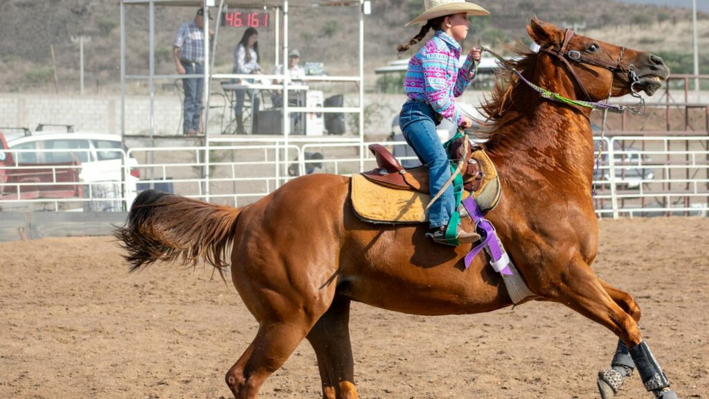 A young cowgirl rides a horse during a rodeo competition at an outdoor arena.