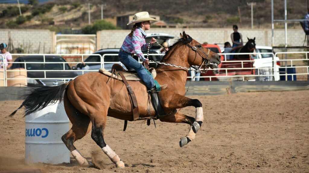 A young girl in a cowboy hat participates in a thrilling barrel racing event, showcasing speed and skill.