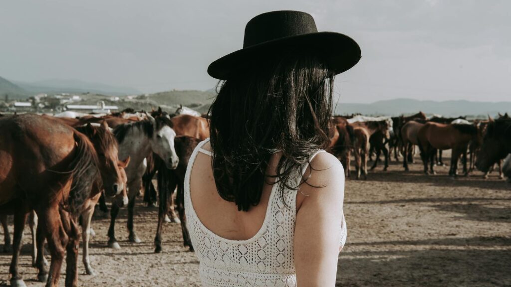 Woman in cowboy hat herding a group of horses in the rural countryside.