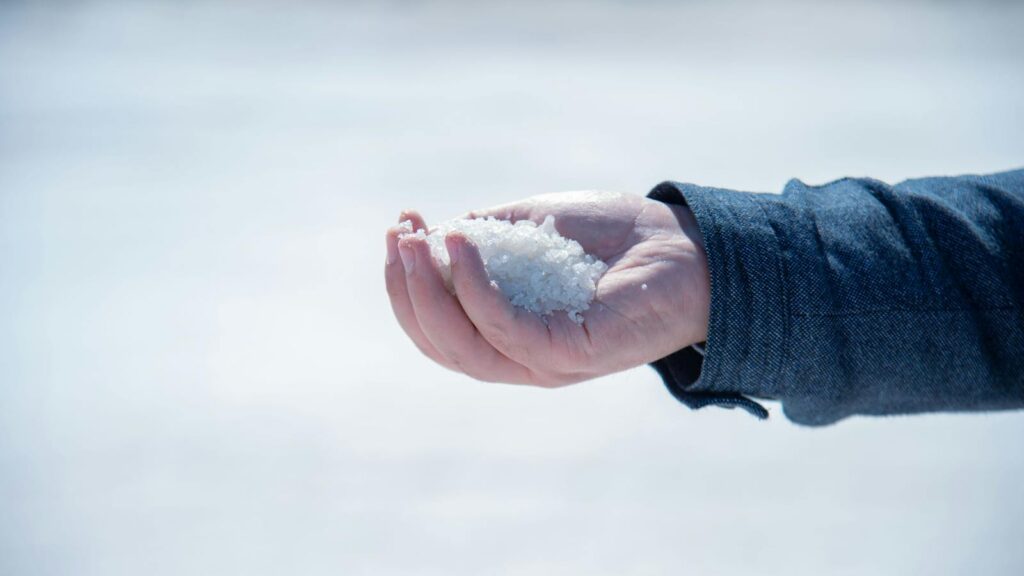 A close-up view of a hand holding white salt crystals outdoors, capturing texture and detail.