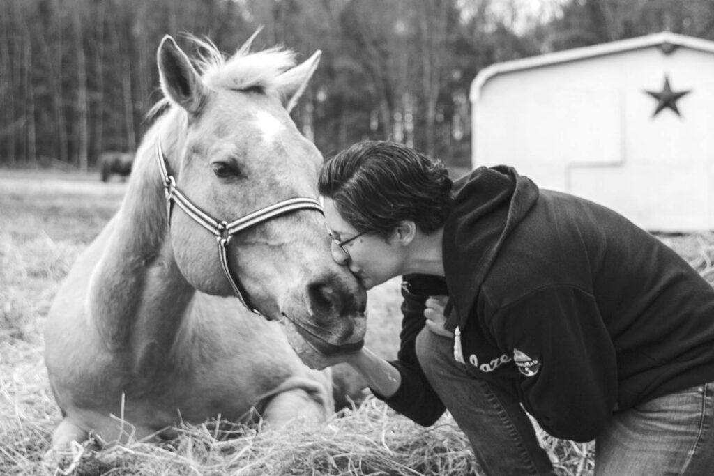 Black and white photo of a woman kissing a horse resting